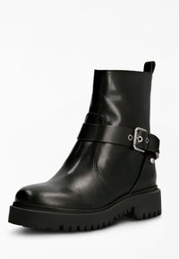 Bottine en cuir noir avec un bout rond, une semelle en caoutchouc épaisse et une sangle décorative avec une boucle en métal. Texture lisse.