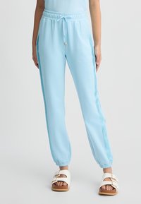 Pantaloni jogger azzurro chiaro con vita elasticizzata, cordoncino e pannelli laterali in rete. Collo a coste alle caviglie e abbinati a sandali bianchi.