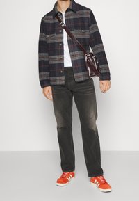 Dark plaid jacket with gray and red accents, white t-shirt, black jeans, and orange sneakers with white stripes, carrying a maroon crossbody bag.