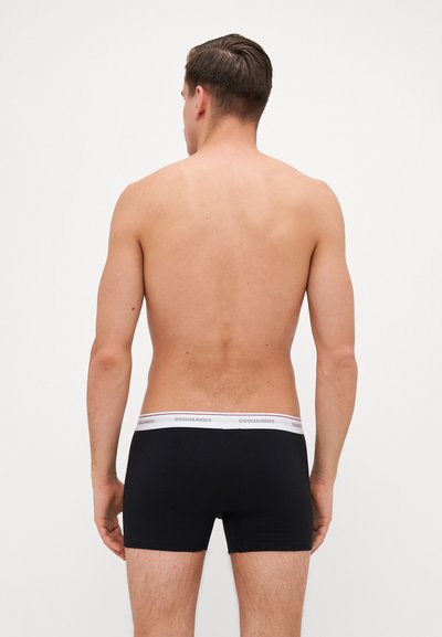 Schwarze Boxerbriefs mit einem weißen elastischen Bund, auf dem das Logo "DSQUARED2" zu sehen ist, von hinten betrachtet, wobei der Stoff und die Passform hervorgehoben werden.