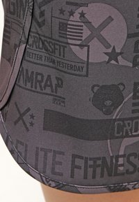 Svarta atletiska shorts i texturerat tyg, med en mängd kontrasterande mönster, logotyper och text i mörkgrå nyanser.