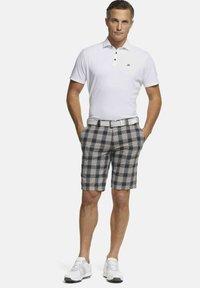 Witte polo met drie knopen, gecombineerd met marineblauwe en crèmekleurige ruitjesshorts. Een witte riem en sportschoenen maken de outfit compleet.
