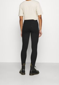 Svarta leggings med hög midja och en slät textur, parat med en ljusbeige t-shirt och svarta snörkängor.