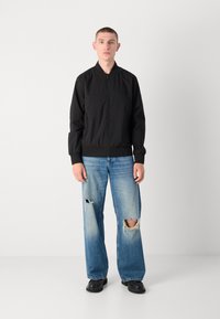Black lightweight bomber jacket with a zip front, ribbed cuffs, and hem, paired with light blue jeans featuring distressed knee openings.