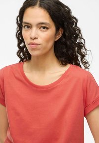 T-shirt in cotone rosso con scollatura ampia, maniche corte arrotolate e una texture liscia, caratterizzato da una vestibilità rilassata e un design semplice.