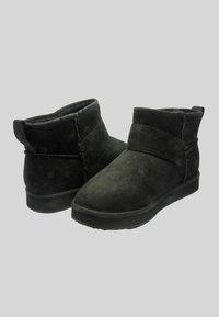 Stivaletti alla caviglia in suede nero con punta arrotondata e risvolto. Suola piatta in gomma con finitura texturizzata, caratterizzata da semplici dettagli di cucitura.