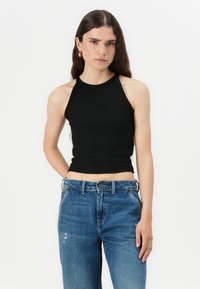 Ribbed black halter top with a fitted design, paired with light blue high-waisted denim jeans featuring subtle distressing.