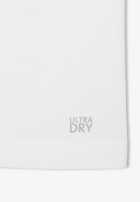 Tejido blanco con dobladillo cosido y pequeño texto gris "ULTRA DRY" impreso cerca del borde inferior.
