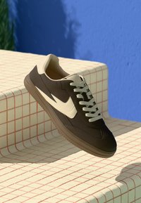 Braune und cremefarbene Sneakers mit einem eleganten Design, ausgestattet mit einem strukturierten Wildleder-Obermaterial, Gummisohle und hellen Schnürsenkeln.