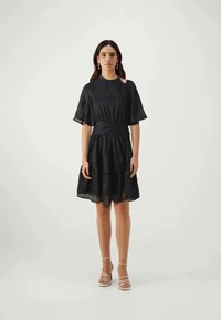 Vestido preto com mangas curtas em forma de sino, cintura franzida e saia em camadas. O tecido tem uma textura subtil com um padrão delicado.