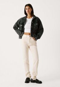 Giubbotto in denim nero, maglietta bianca a corti, pantaloni crema e mocassini neri. Caratteristiche includono tasche, chiusure con bottoni e una vestibilità comoda.