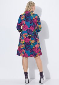 Wielokolorowa sukienka z żywym wzorem kwiatowym na niebieskim tle, z długimi rękawami i długości do kolan. Udekorowana zapięciem na zamek.