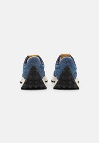 Zapatillas de ante azul con tejido texturizado, una entresuela blanca y suela de goma negra con forma triangular y puntos elevados para un mejor agarre.