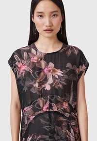 Top a maniche corte con motivo floreale nero, caratterizzato da grandi orchidee rosa e marroni, con una texture morbida e trasparente e scollo arrotondato.