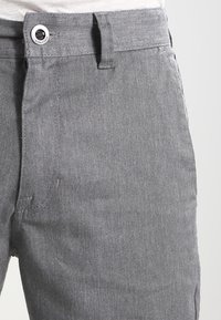 Pantalons en denim gris avec fermeture à bouton et passants de ceinture, offrant une texture lisse et un léger stretch, mettant l'accent sur le confort et l'ajustement.