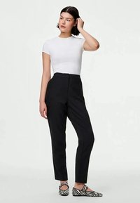 Calças pretas ajustadas com um cintura alta, perna reta e pregas discretas. Combinadas com uma t-shirt branca justa e sapatos slip-on às riscas.