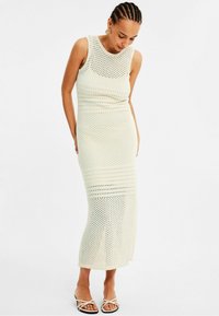 Knit midi-mekko off-white-värissä, jossa on teksturoitu muotoilu, ja se on varustettu tiukalla vartalolla ja levenevällä helman muodolla. Yhdistetty mustiin sandaaleihin.