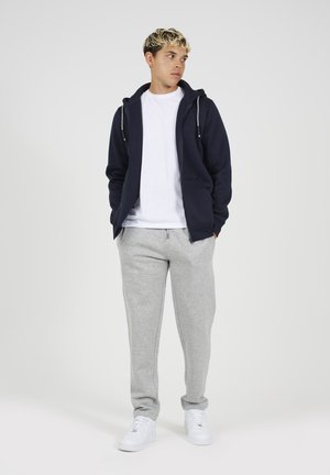 Sweatshirt zippé marine, t-shirt blanc, pantalon de survêtement gris et baskets blanches. Tenue décontractée, tissu texturé, avec des accents de cordon de serrage sur le sweatshirt.
