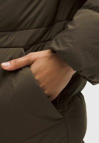 Kurtka puchowa w kolorze oliwkowej zieleni z boczną kieszenią. Rękaw ma marszczoną fakturę, z wytłoczonym logo na mankiecie. Miękki, lekki materiał.