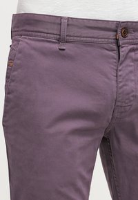 Fioletowe bawełniane spodnie o gładkiej fakturze, z zapięciem na guzik, szlufkami na pasek oraz przednimi i tylnymi kieszeniami.