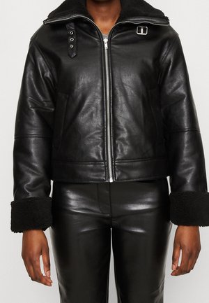 Sort læderjakke med et cropped design, lynlås-lukning og store sorte shearling-manchetter. Har trykknapper og en foret krave.