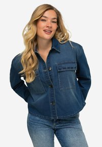 Giacca in denim con chiusura frontale a bottoni, due tasche sul petto, maniche lunghe e orlo leggermente accorciato in un blu medio.