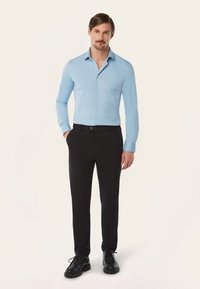 Lichtblauwe blouse met lange mouwen en een button-down kraag, gecombineerd met zwarte slim-fit broek en zwarte schoenen. Glad textuur, getailleerd ontwerp.