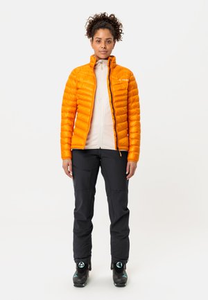 Leuchtend orangefarbene Steppjacke mit horizontalem Steppmuster, getragen über einem hellen Oberteil und kombiniert mit schwarzen Skihosen und Stiefeln.