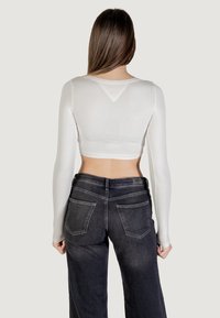 Biały, długi rękaw, krótki top z okrągłym dekoltem, w połączeniu z wysokim stanem ciemnych dżinsów z tylnymi kieszeniami.