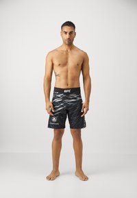 Black UFC shorts with a wave pattern, featuring a logo on the waistband and another on the side, made of a lightweight synthetic material.