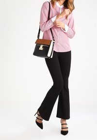 Borsa nera con una patta e un gancio beige, blusa a righe rossa e bianca, pantaloni neri svasati e tacchi neri con cinturini alla caviglia.