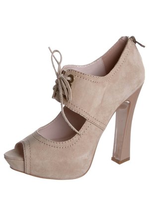Chaussure à talon haut en daim beige avec bout ouvert, laçage sur le devant, côtés découpés et fermeture éclair au talon.