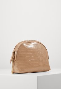 Busta beige in similpelle con texture a coccodrillo, forma arrotondata e dettaglio con catena dorata. Dotata di chiusura superiore con cerniera.