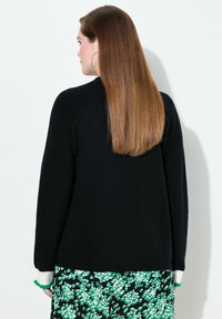 Pull en tricot noir avec une texture côtelée, doté de manches longues et d'accents contrastants blancs et verts aux poignets, vu de dos.