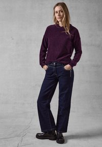 Felpa a cappuccio in corduroy viola, abbinata a jeans in denim a gamba larga blu scuro con tasche laterali e stivali chunky neri. Outfit casual.