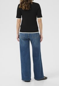 Top corto de manga corta negro acanalado con detalles en blanco, combinado con unos vaqueros de denim azul de pierna ancha, mostrando el diseño trasero y los detalles de los bolsillos.