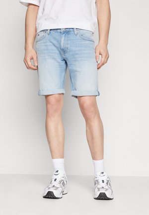 Shorts de mezclilla azul claro con dobladillos enrollados, terminados con un botón frontal y cremallera. Usados con calcetines blancos y zapatillas.