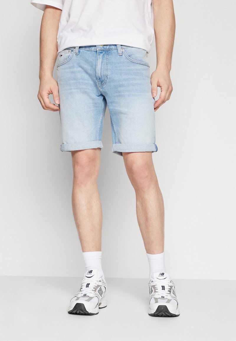 Shorts de mezclilla azul claro con dobladillos enrollados, terminados con un botón frontal y cremallera. Usados con calcetines blancos y zapatillas.