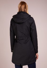 Schwarze wasserdichte Jacke mit tailliertem Schnitt, Kapuze und gesteppter Kragen. Verfügt über eine glatte Textur und lange Ärmel mit Knopfdetails.