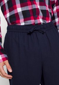 Marineblaue Hose mit elastischem Bund und Kordelzug, kombiniert mit einem rot, schwarz und weiß karierten Hemd mit Knopfverschluss.