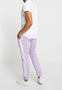 Lila joggers med vita ränder längs sidorna, designade i slim-fit stil. Kombineras med en vit t-shirt och vita sneakers.