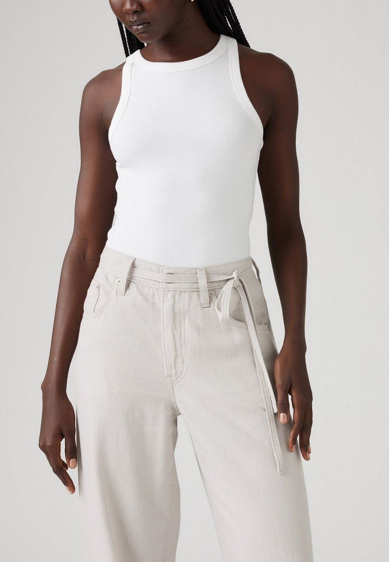 Top corto bianco a costine con scollo rotondo, abbinato a pantaloni beige chiaro a vita alta con cintura annodata e tasche frontali.