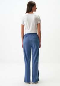 Niebieskie spodnie sportowe z elastycznym paskiem w talii i tylną kieszenią, w zestawie z białą bluzką z krótkim rękawem. Gładka tekstura, luźny krój.