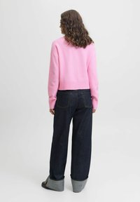 Izrezan roza pulover z dolgimi rokavi, izdelan iz mehke tkanine. Združen z temno jeans širokimi hlačami z zavihanimi robovi.