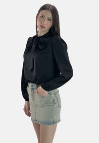 Sort satinbluse med en sløjfedetalje, puffede lange ærmer, parret med en lys denim mininederdel, der viser en afslappet stil.