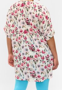 Lehká květinová tunika v krémové barvě s růžovými a modrými květinami, krátkými rukávy, volným střihem a mírně zakřiveným lemem; doplněná tyrkysovými legínami.