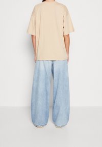 Beige oversize tričko s kulatým výstřihem a krátkými rukávy, v kombinaci s světle modrými širokými džínami s vybledlým vzhledem a ohrnutými nohavicemi.