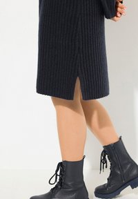 Robe en tricot bleu marine foncé avec des côtes verticales, fente sur le côté, accompagnée de bottes de combat noires à lacets avec une finition texturée et des semelles épaisses.