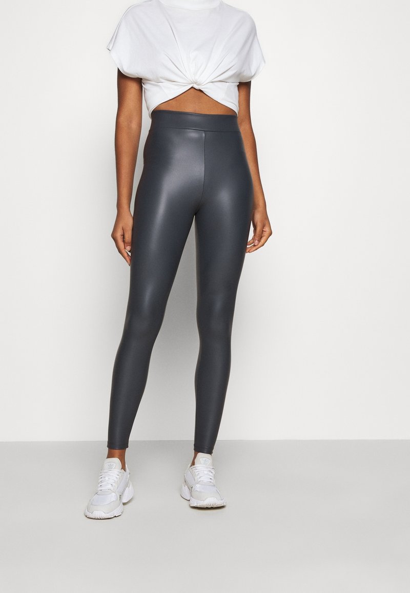 Leggings gris taille haute à finition brillante, associés à un crop top blanc noué et des baskets blanches, mettant en valeur une silhouette épurée.