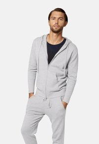 Felpa grigia con zip e pantaloni della tuta coordinati. Tessuto morbido, design aderente, tasche frontali e cordino regolabile in vita.